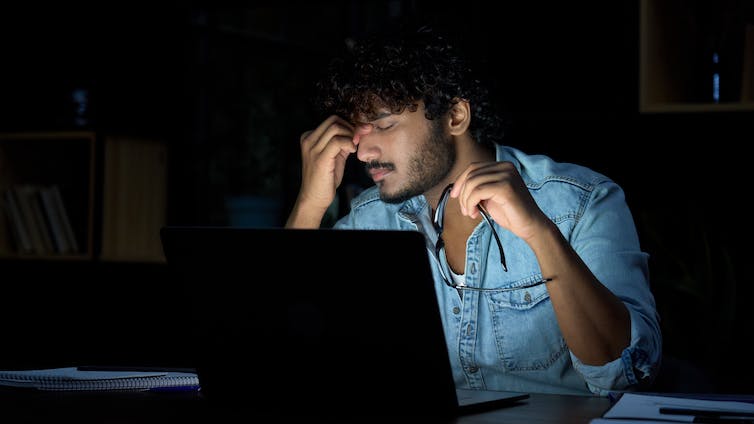 A stressed man in front of a laptop puts his fingers on his forehead